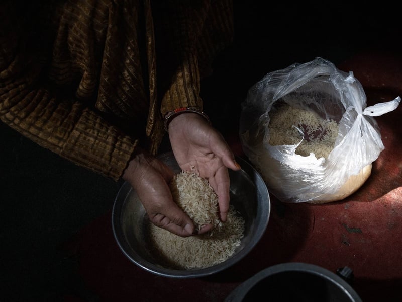 A woman's hands hold a handful of rice above a metal bowl.