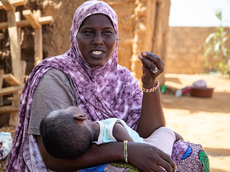 A woman in a purple headscarf holding her sleeping child.