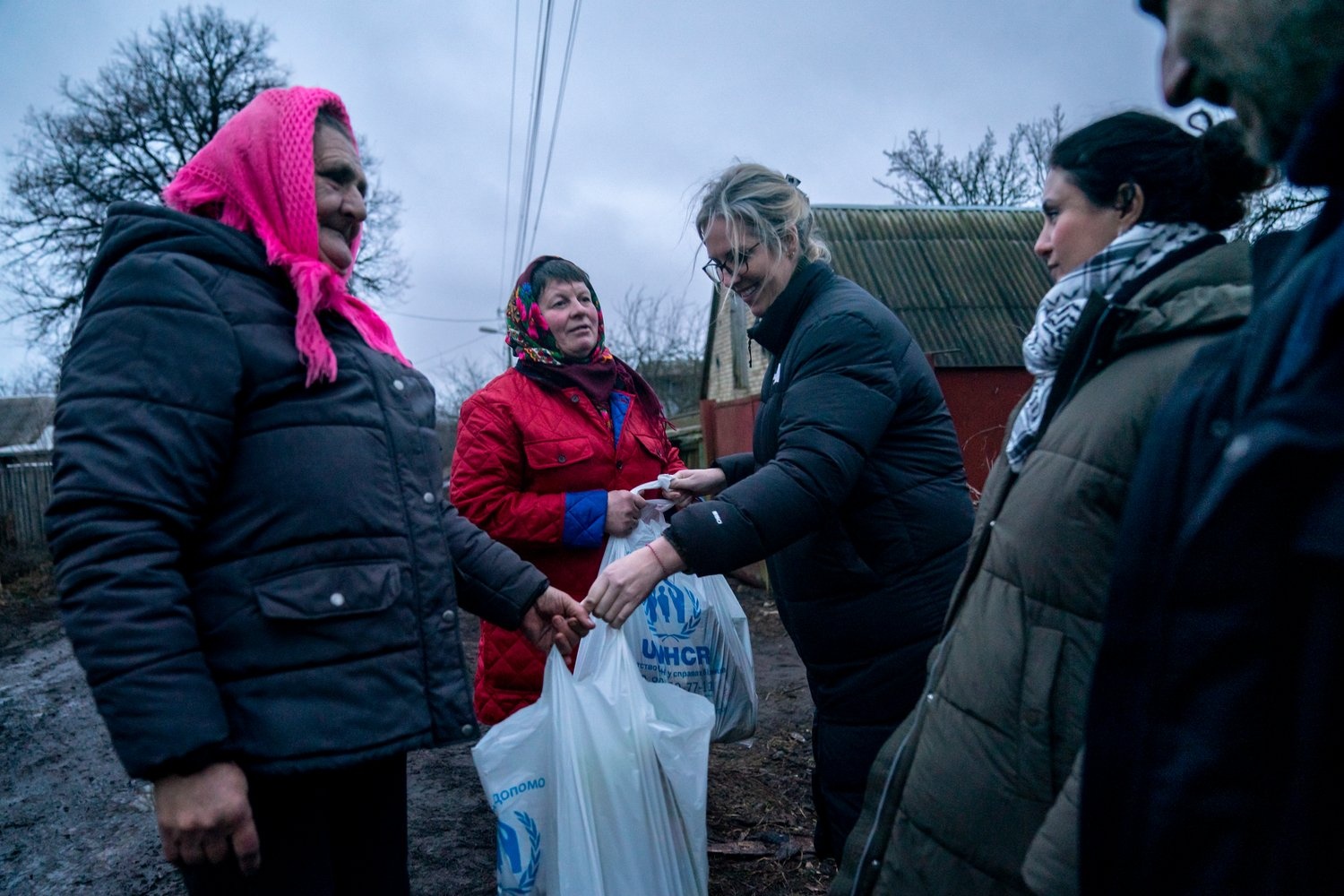 Two Ukrainian women receive bags of food and other aid items from members of UNHCR staff.