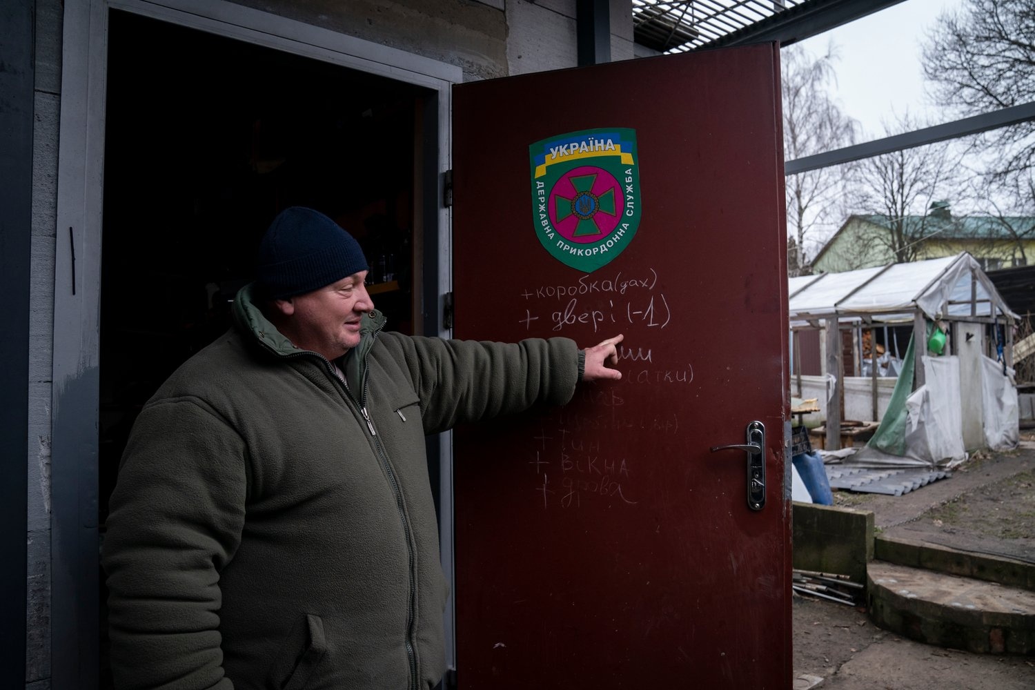 A man points to repair plans written in chalk on the front door of his house.