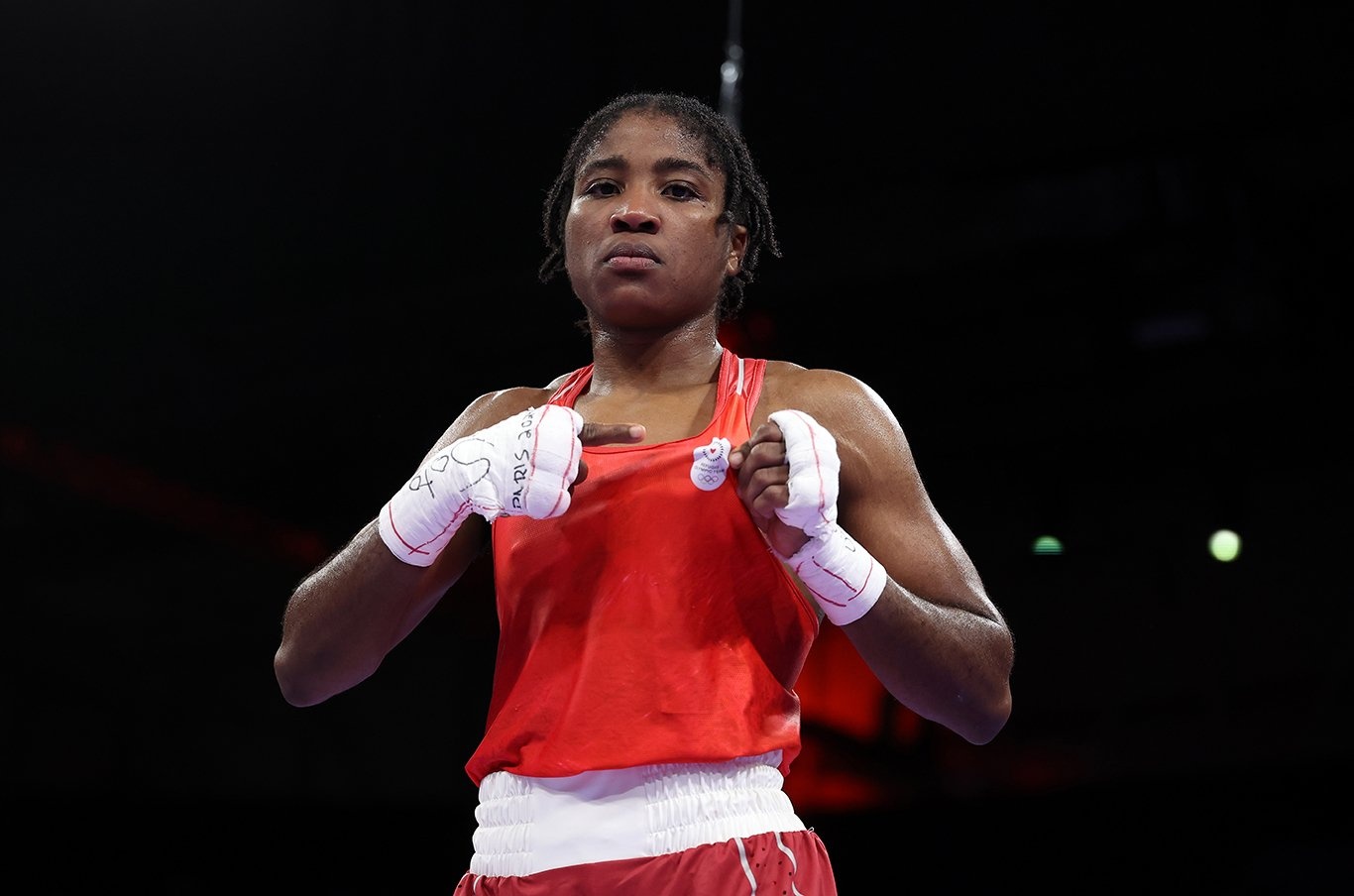 Cindy Ngamba poses for a photo in boxing gear, pointing at the Refugee Olympic team logo on her clothes.