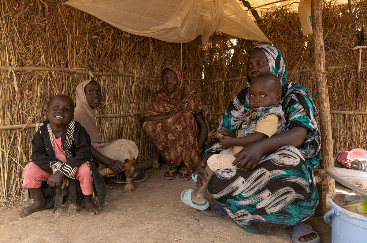 A woman and four children sit smiling inside a shelter