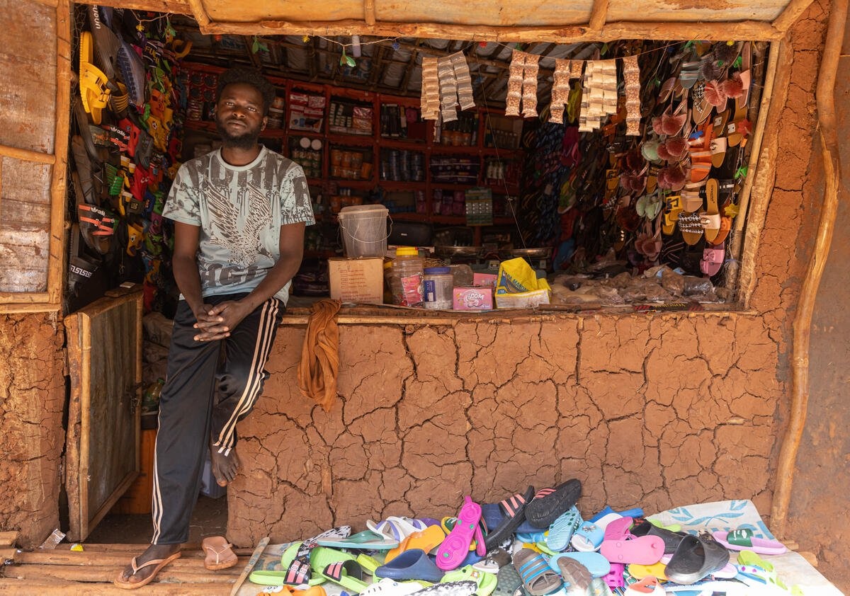 A Sudanese man outside his small shop, with a pile of sandals out the front at his feet