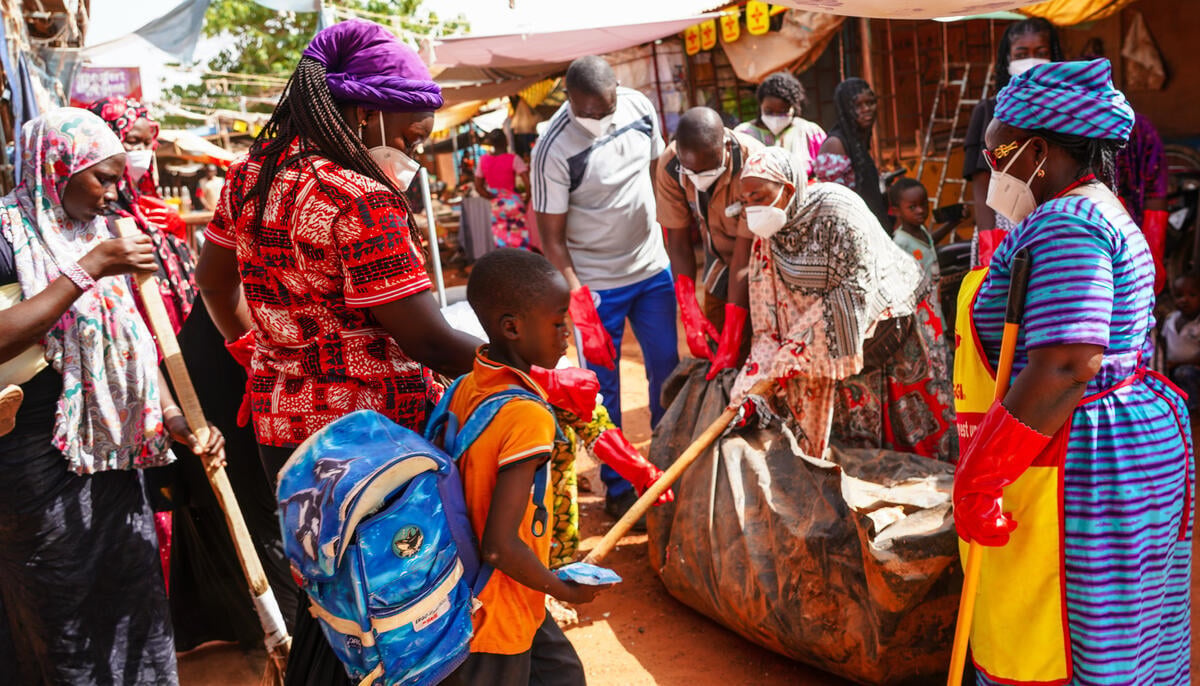 A group of colourfully dressed refugees help to clean an outdoor market.