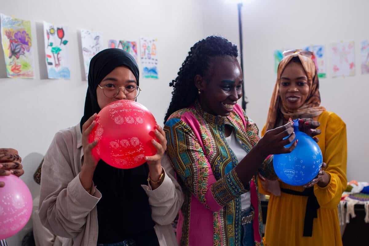 Three women blow up balloons.