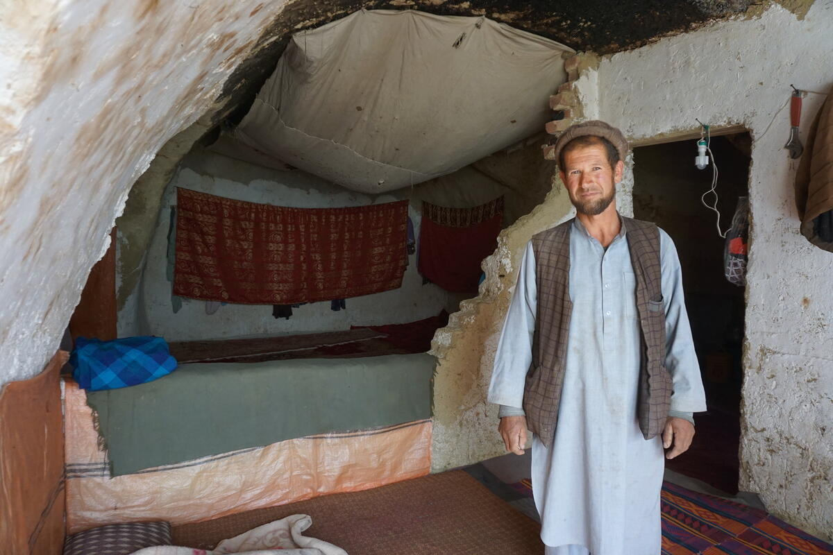 A man stands inside his bedroom in a cave where he lives with his family.