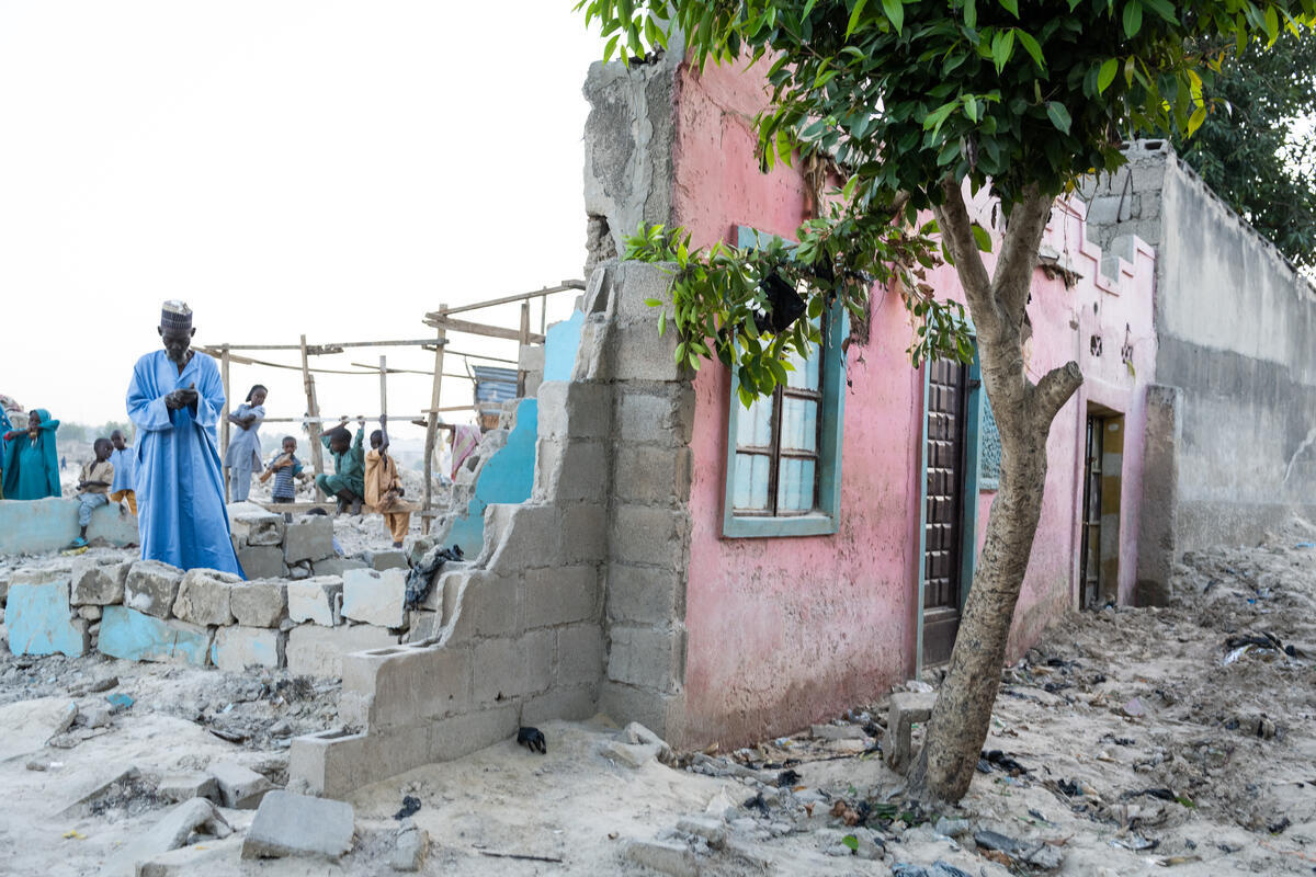 A man stands in the ruins of a house, only the facade of which is still standing.
