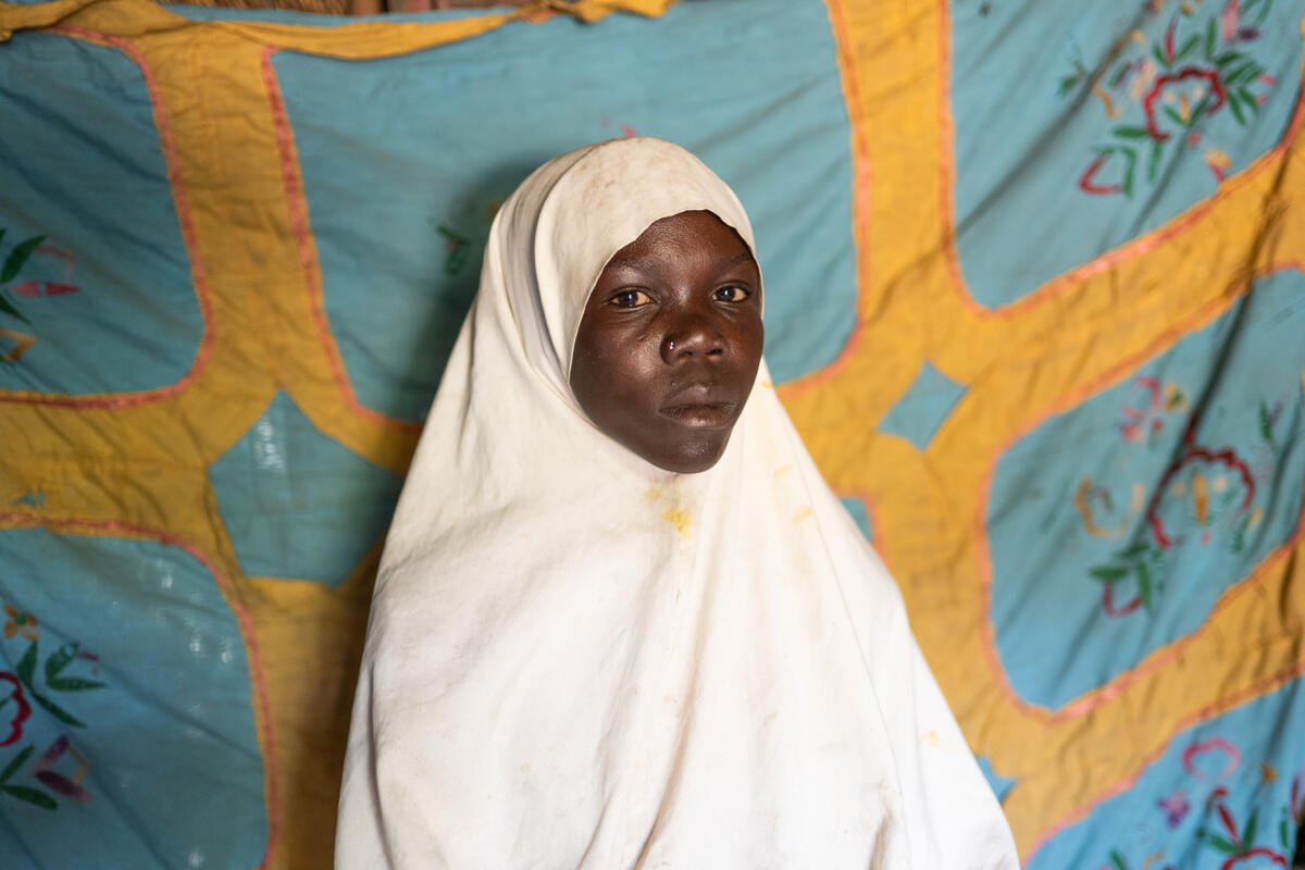 A girl in a white headscarf stares at the camera.