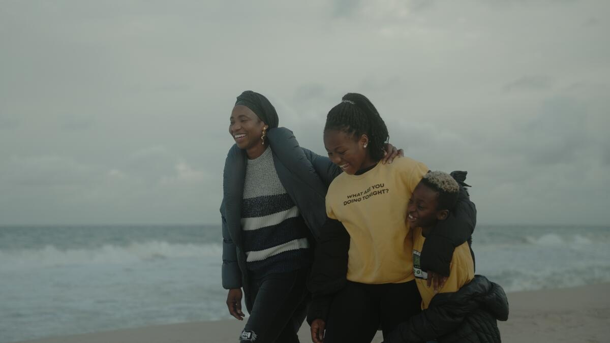 A mother, daughter and son walk arm in arm along a sandy beach on a cloudy day.