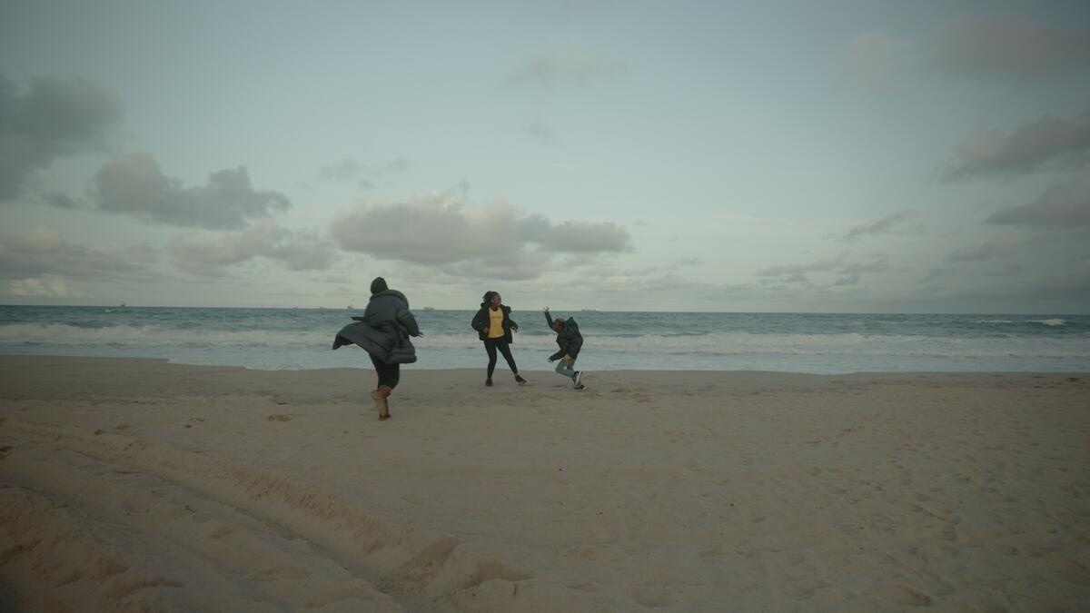 Three people run and play by the shore of a deserted beach.