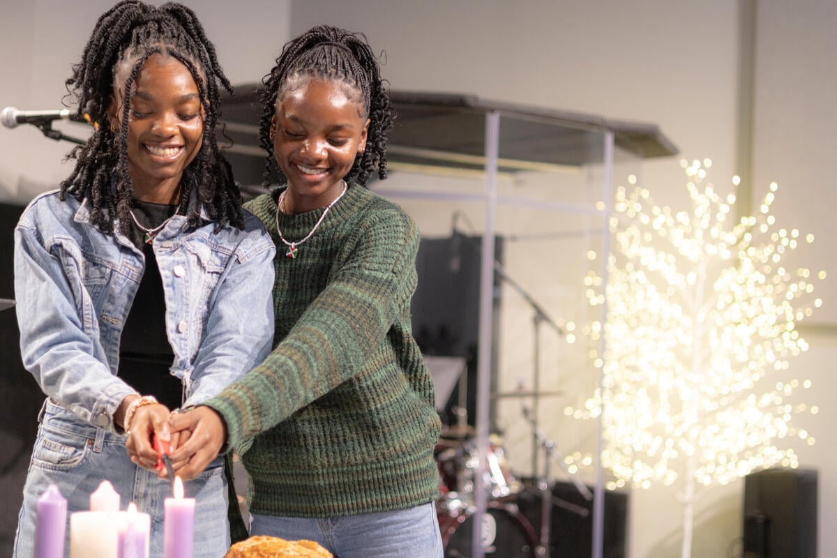 Two young sisters smile as they light a candle together.