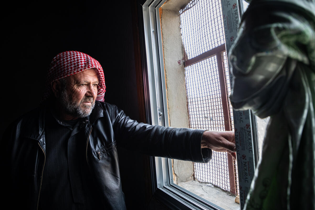 A man in a red headscarf stands beside a window.