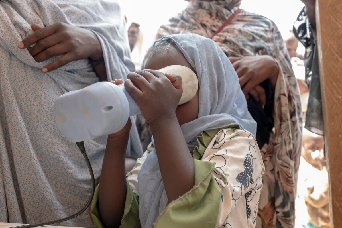 A young girl holds a biometric registration device over her eyes as others queue behind her.