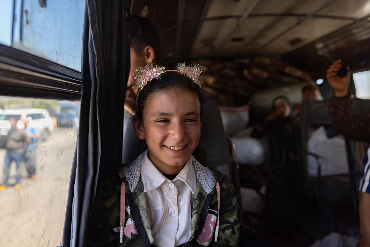 A smiling girl sits next to the window on a bus.