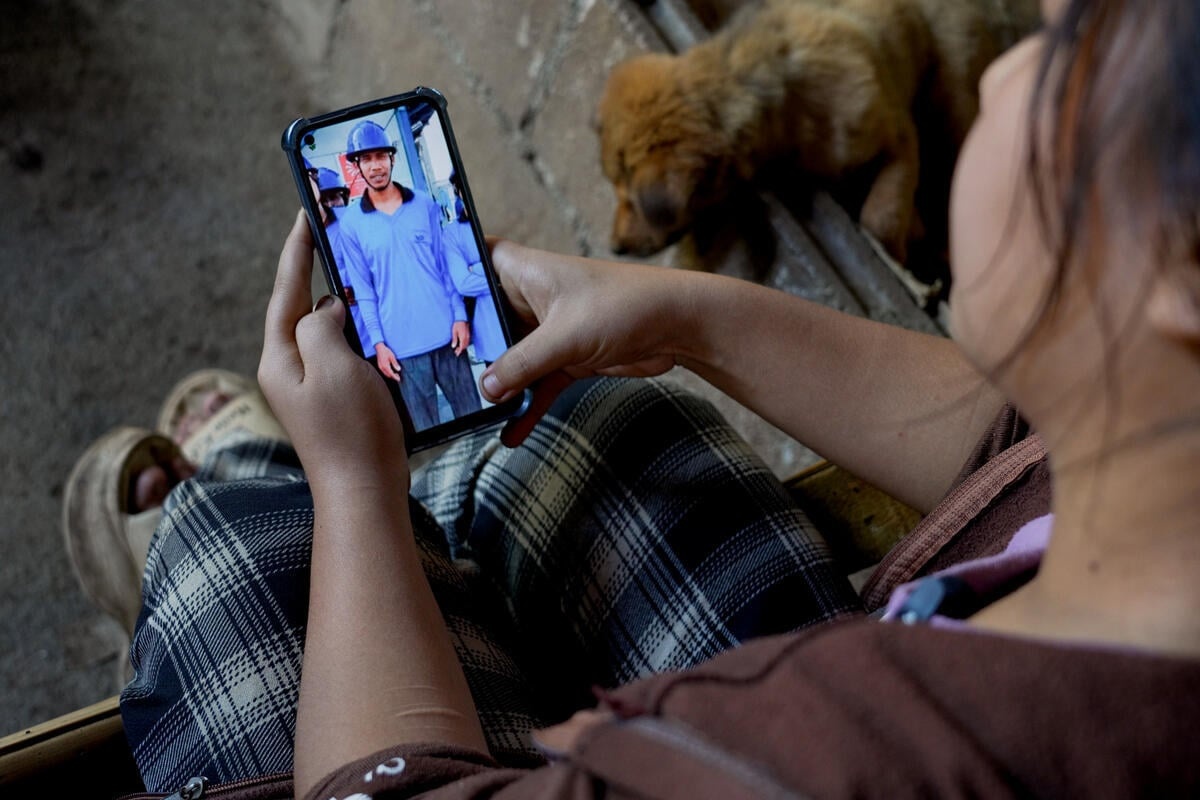 A woman looks at a photo of a man in a blue uniform and hard hat on her mobile phone