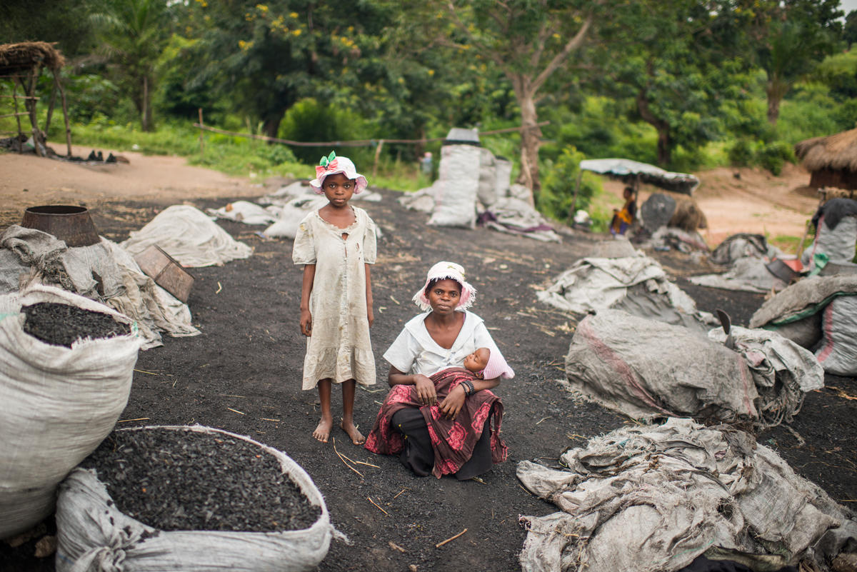 Surrounded by bags of coal they have packed, a displaced Congolese woman poses for a photo with her two children.