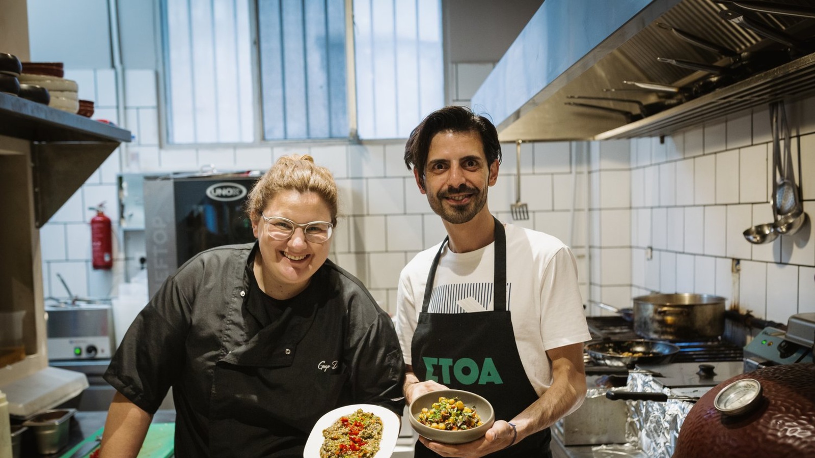 Two men hold two dishes in a professional kitchen.