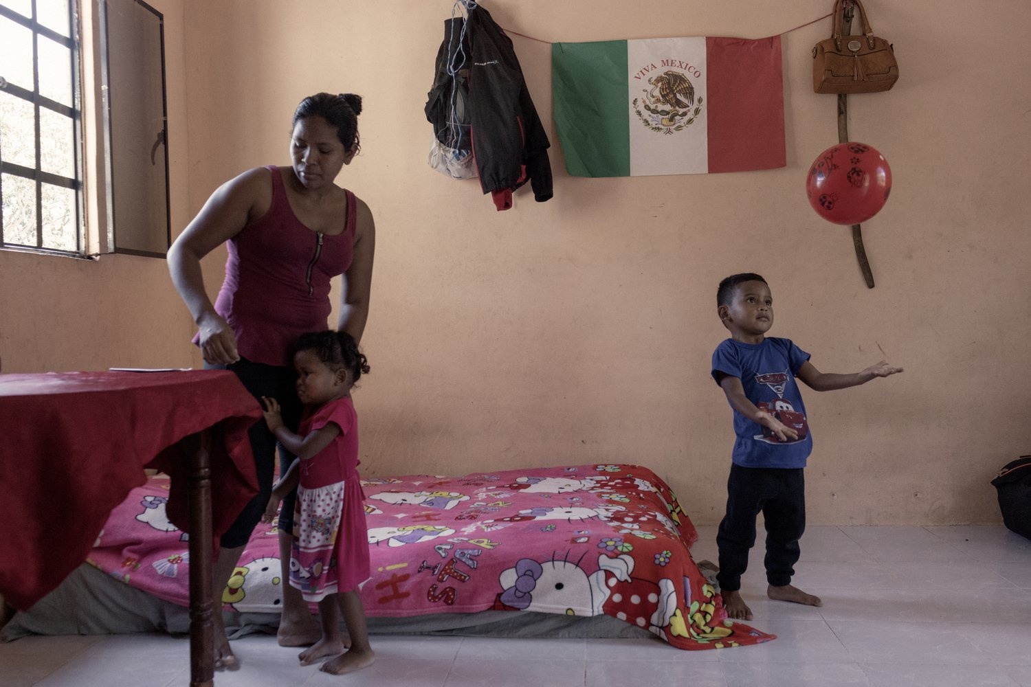 A woman tends to a small girl while a young boy plays with a red ball.