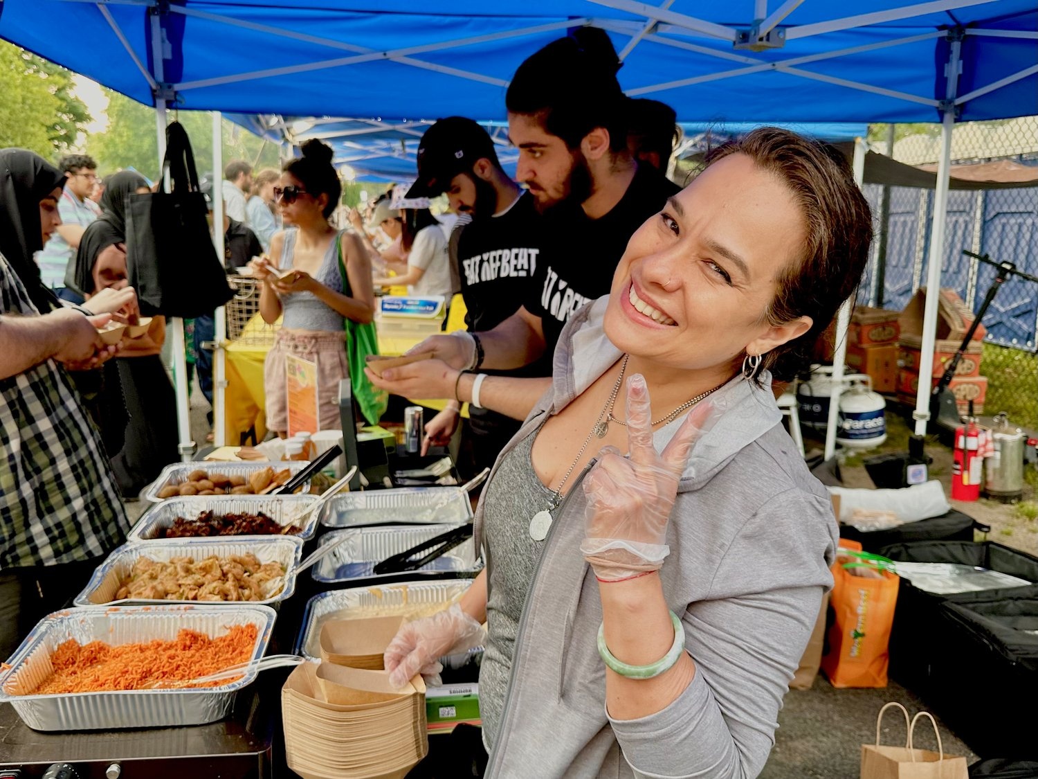 A woman makes the peace sign while she and others serve food from a stall.