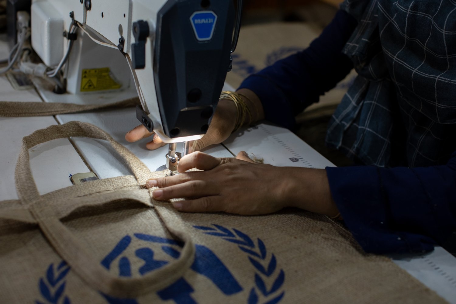A woman uses a machine to sew a UNHCR bag made from jute.