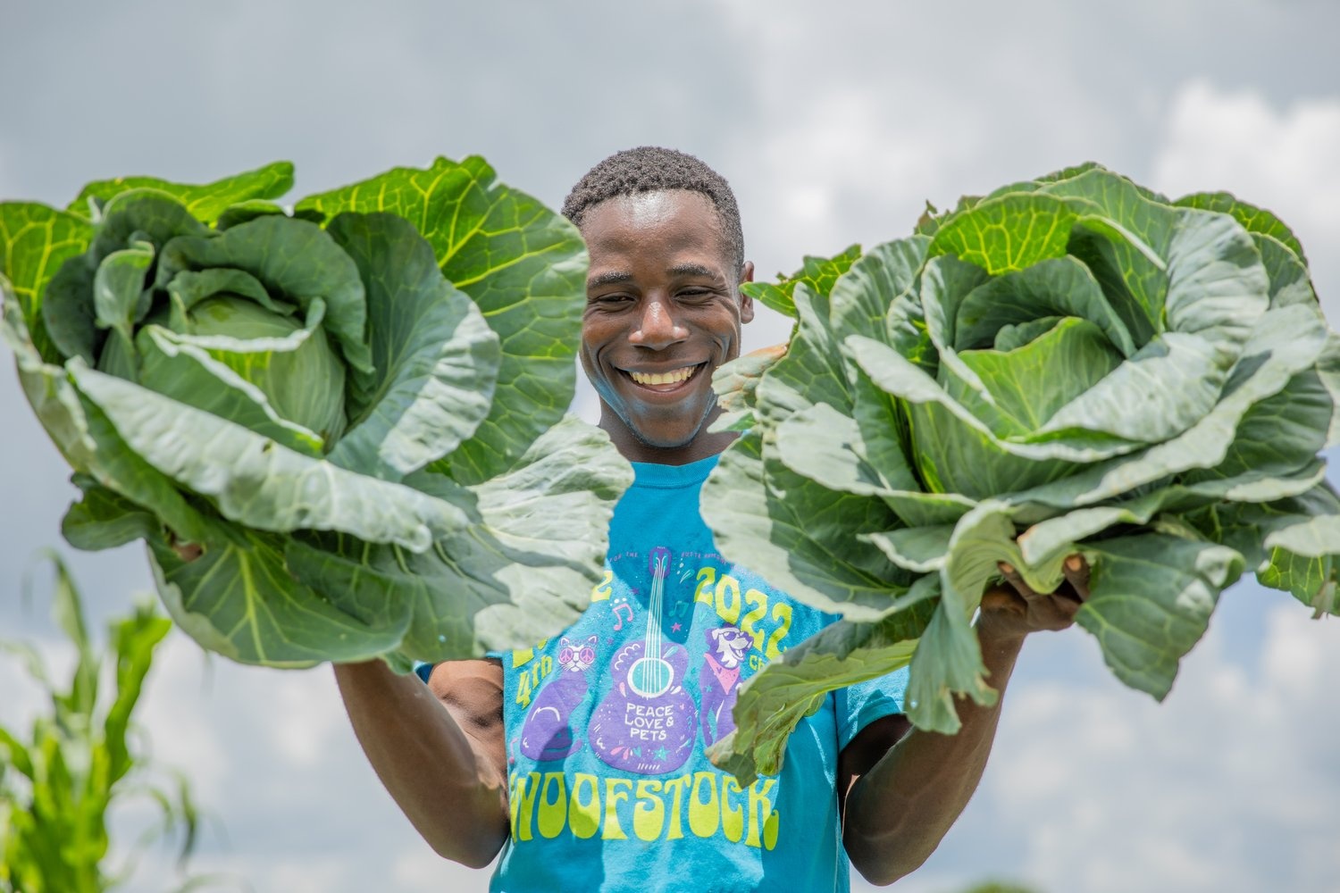 A smiling young man holds up two large cabbages.