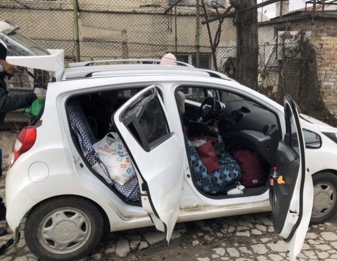 A small white car with its doors and trunk open is full of luggage