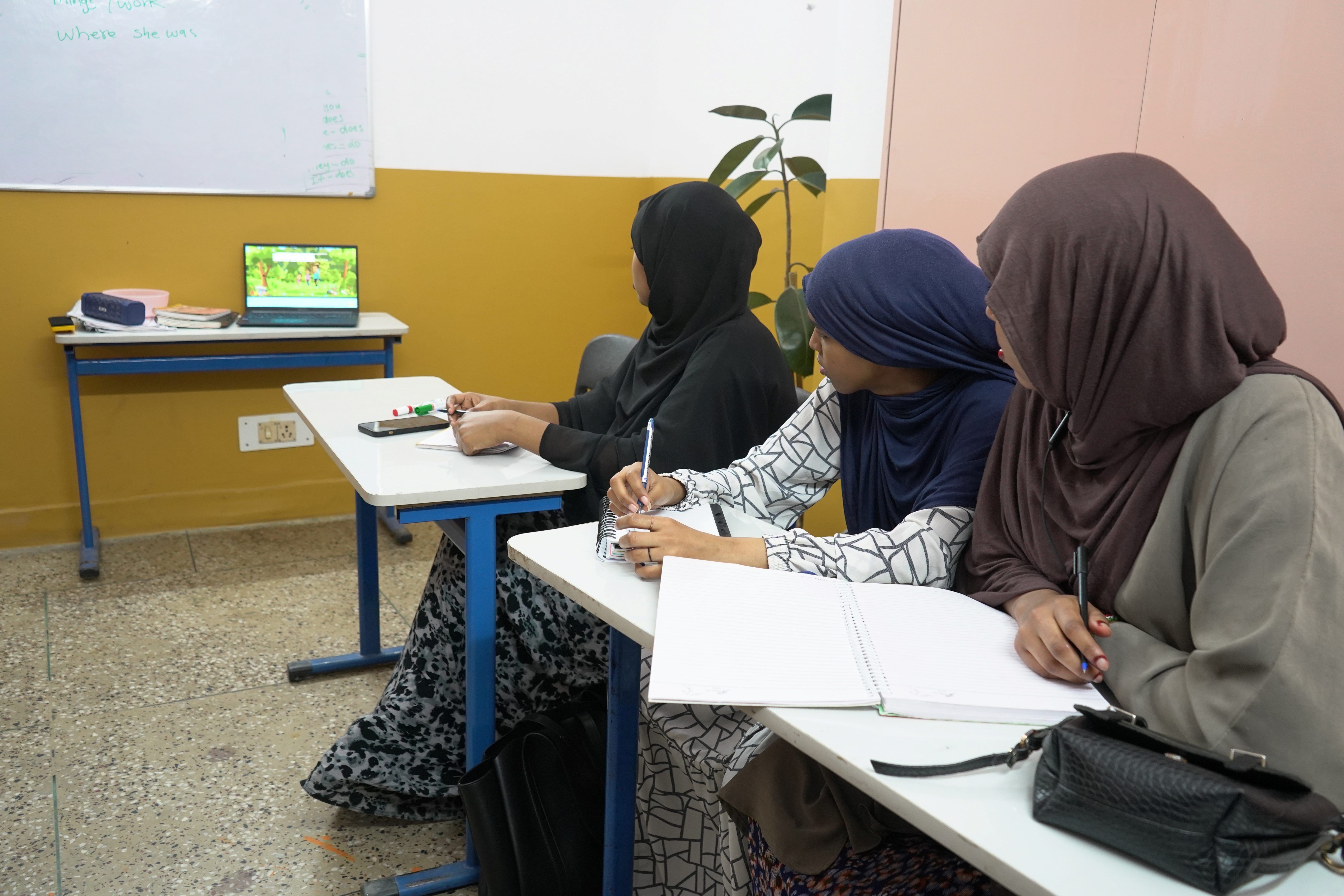 Students repeat phrases from an English-learning video, helping each other improve pronunciation in a lively youth club session.