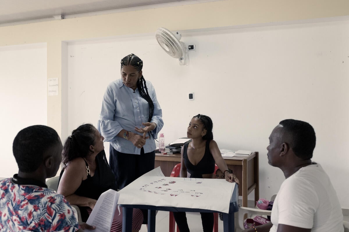 A woman talks to people sitting around a table in a classroom.