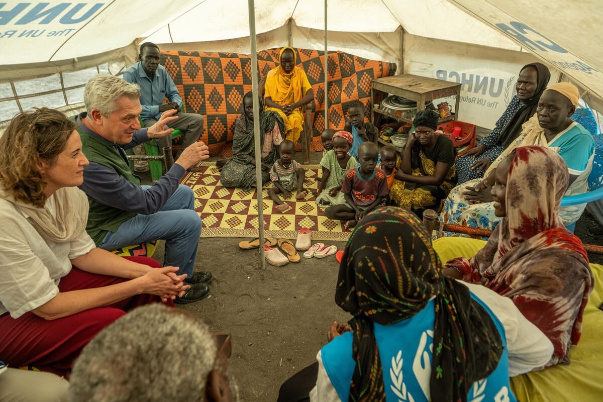 UN High Commissioner for Refugees Filippo Grandi seated in a circle with a large refugee family inside a UNHCR tent.