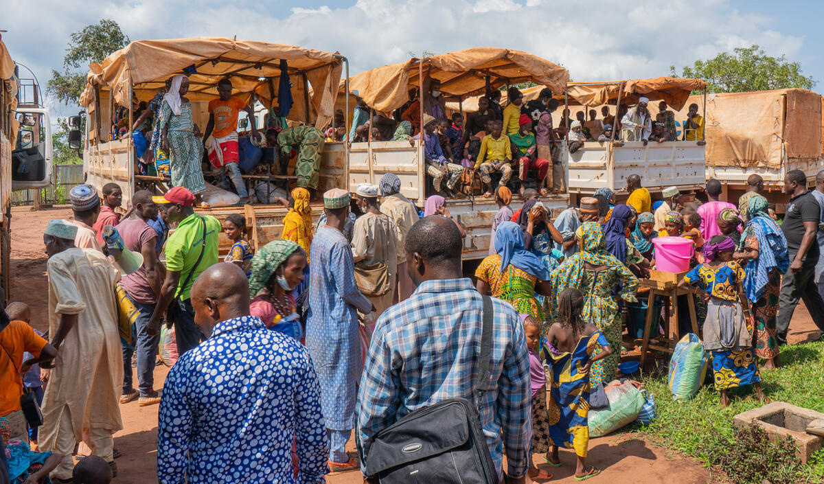 A crowd of people gathers behind several trucks filled with passengers