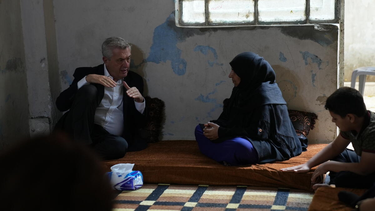 A man and a woman sit talking on a mattress on the floor beneath the window in the room of an apartment