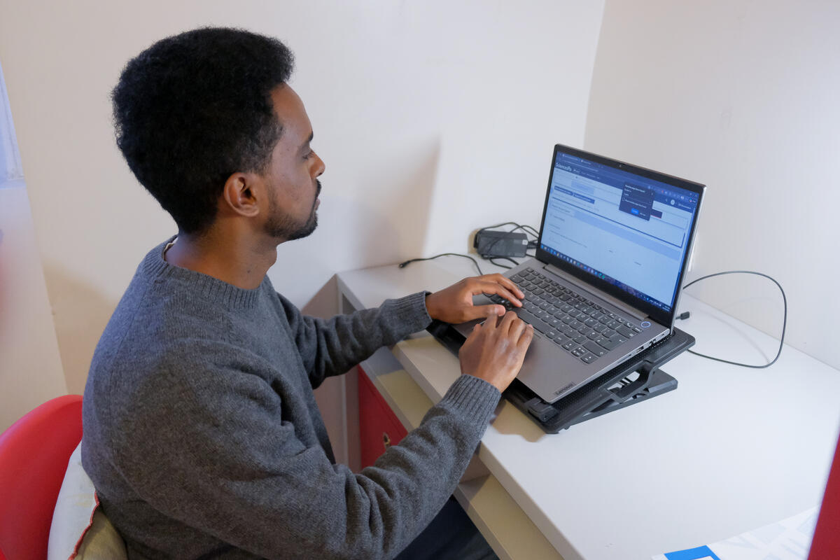 A man sits at a small desk working on a laptop.