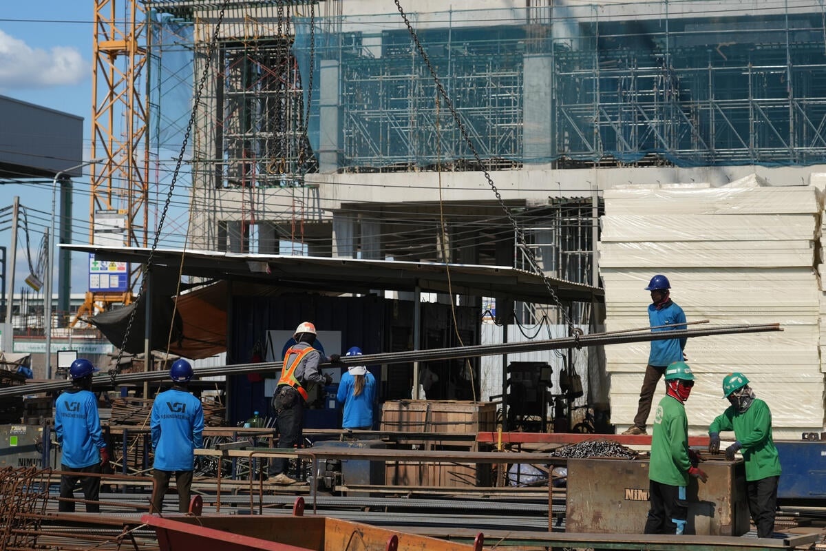 A group of workers in blue and green uniforms work on a construction site
