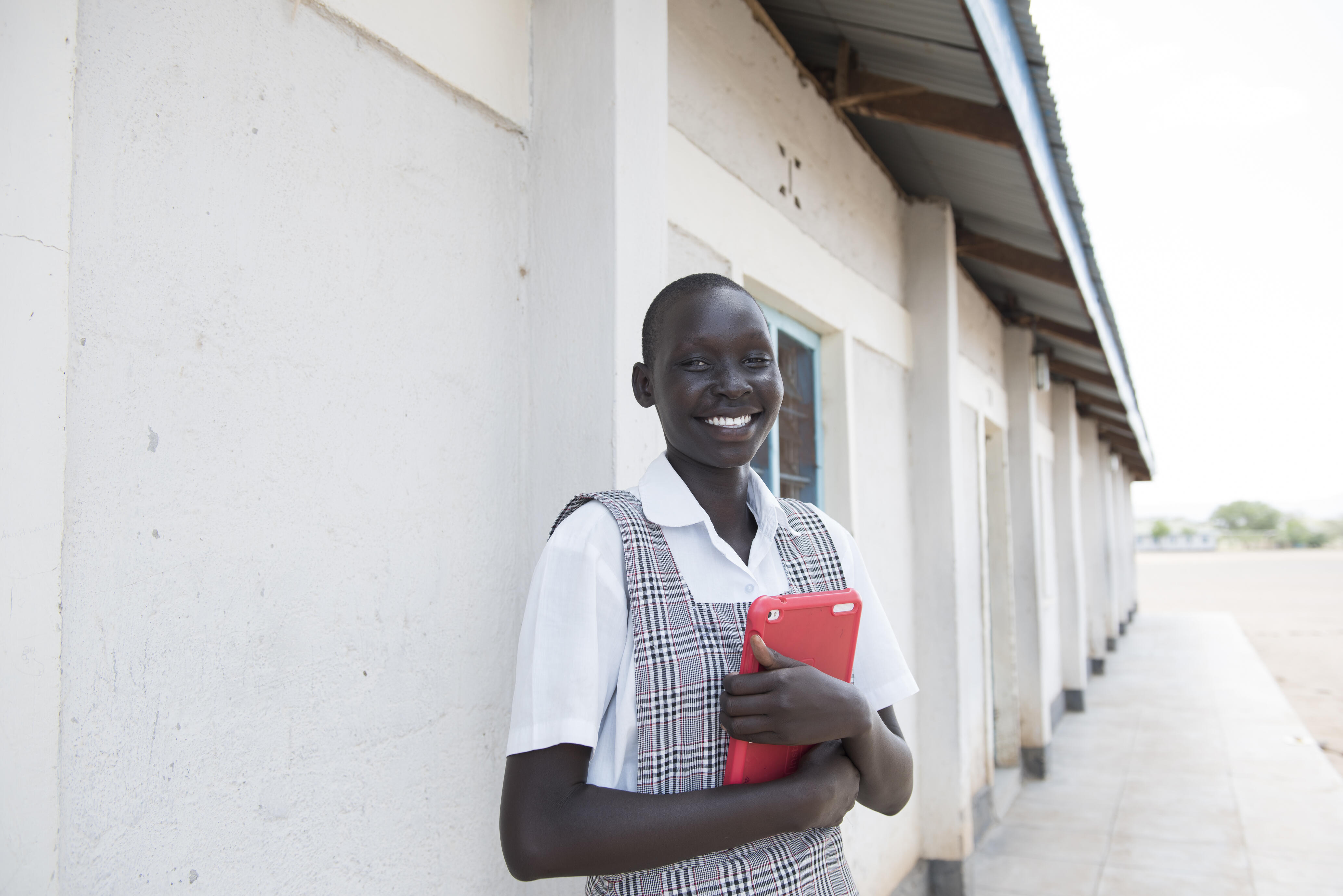 Kenya. Mary standing outside school holding a tablet