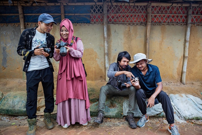 Four adults, two standing and two sitting, each examine a camera. 