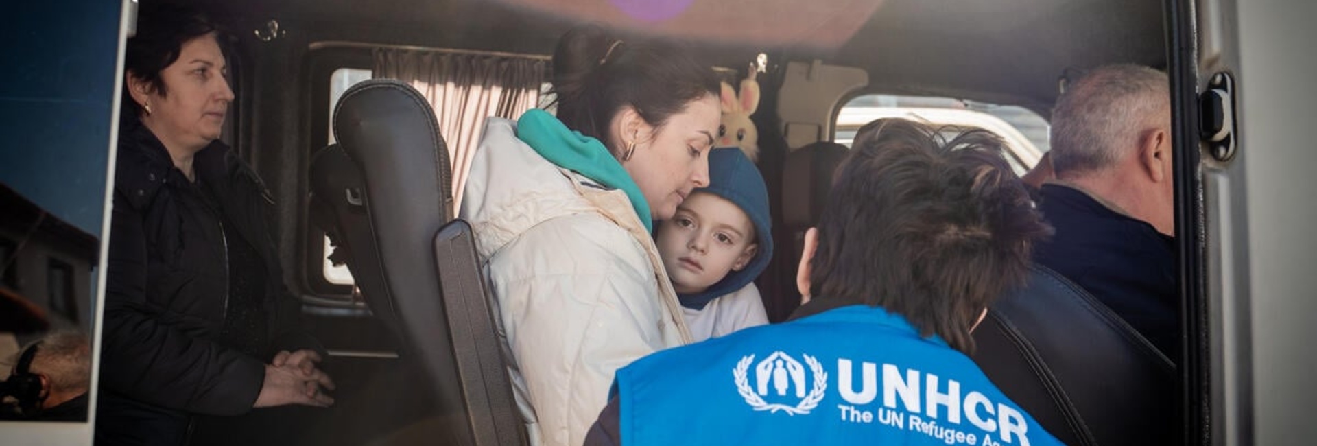A UNHCR staff member speaks with a Ukrainian refugee mother and young boy on a bus.