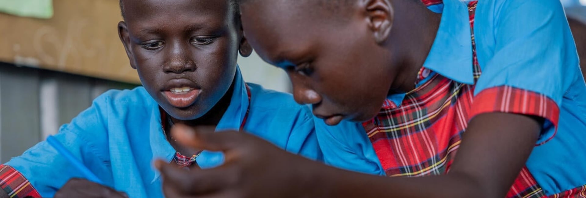 Two South Sudanese students sit together at a desk, concentrating on their work.
