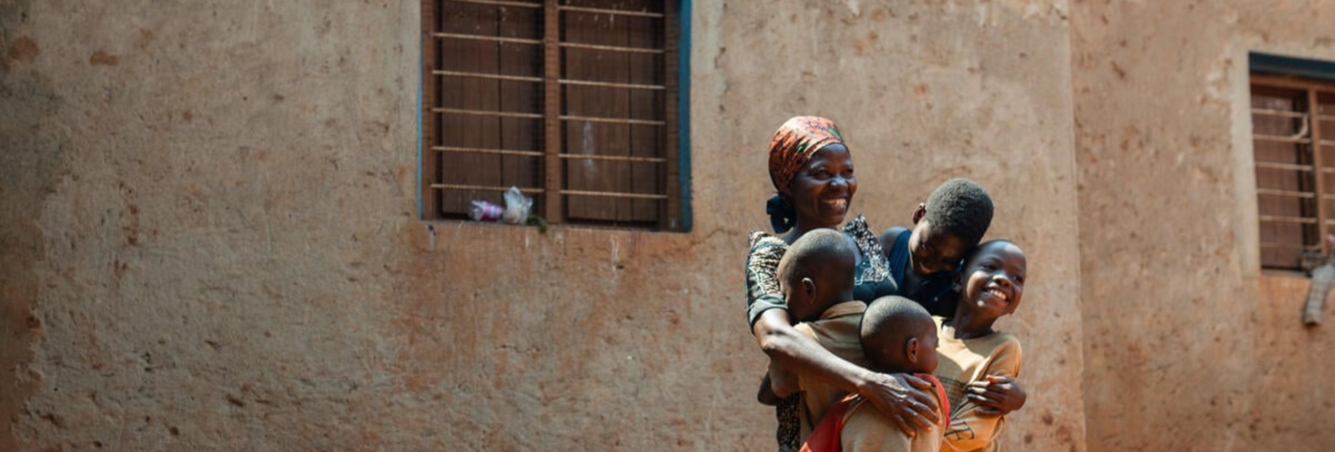 A Burundian woman hugs four of her children standing outside a building with a huge smile on her face