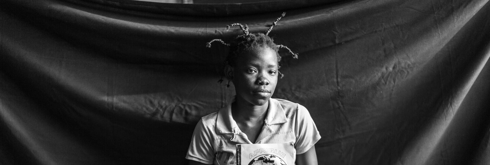 Thirteen–year-old Fideline holds one of the school notebooks that she was able to salvage when she and her family fled for their lives and boarded a boat to Batanga.