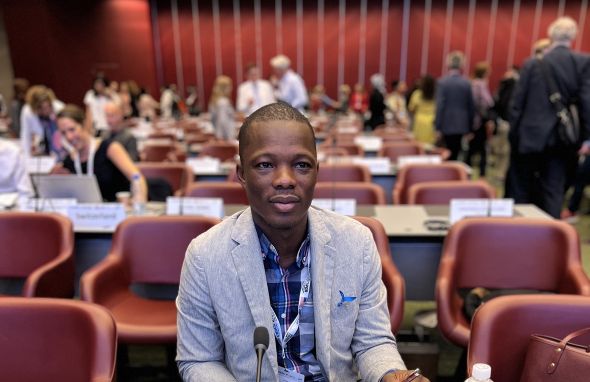 A man sits in a conference room with other delegates in the background.