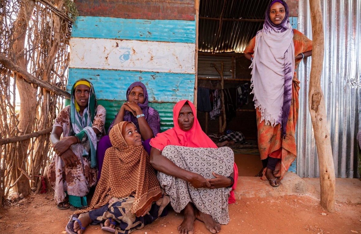 A group of women sit and stand outside a shelter.