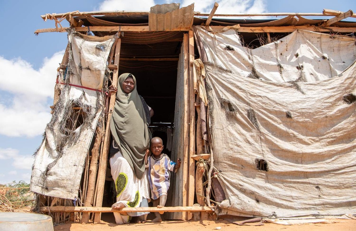 A woman and her young child stand in the entrance of a makeshift shelter.