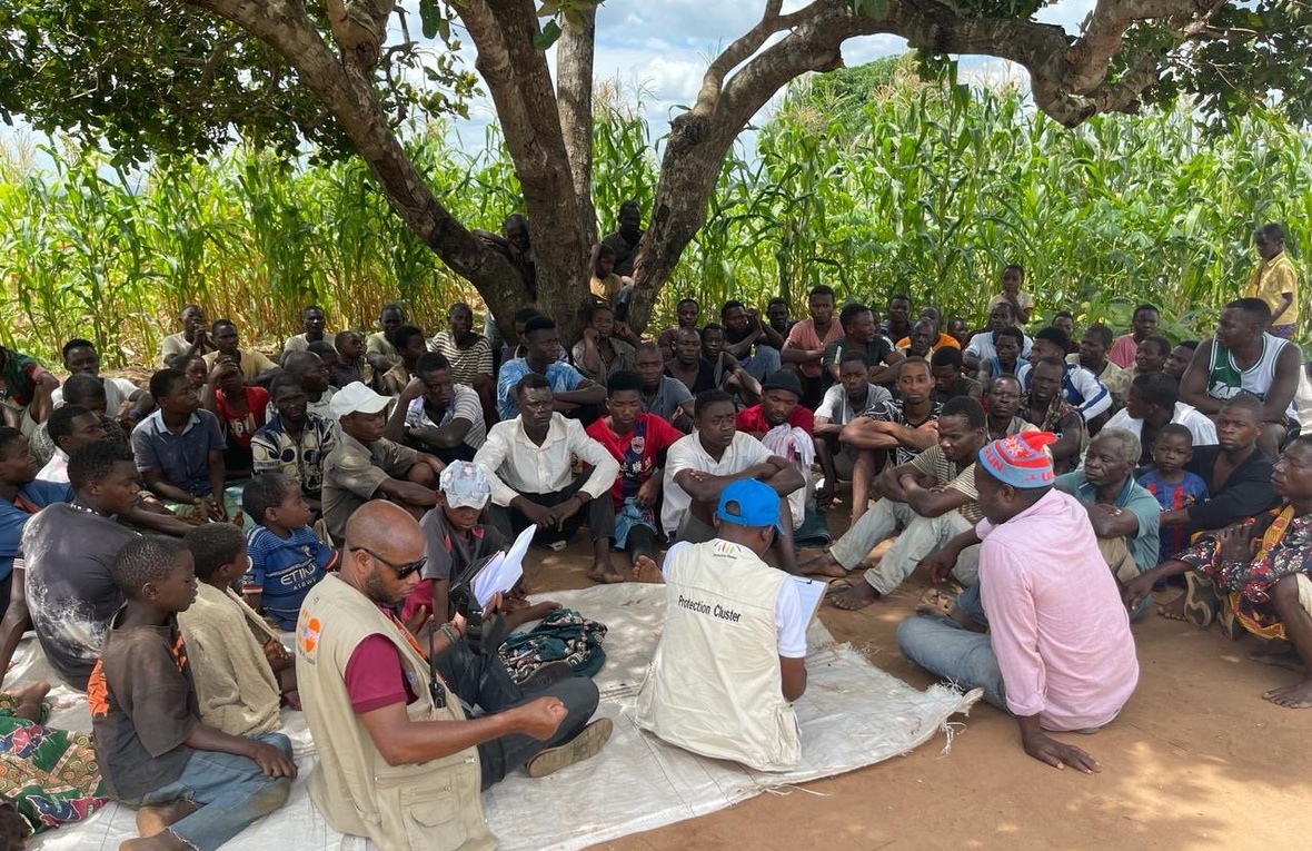 UNHCR staff and refugees sit together under a tree