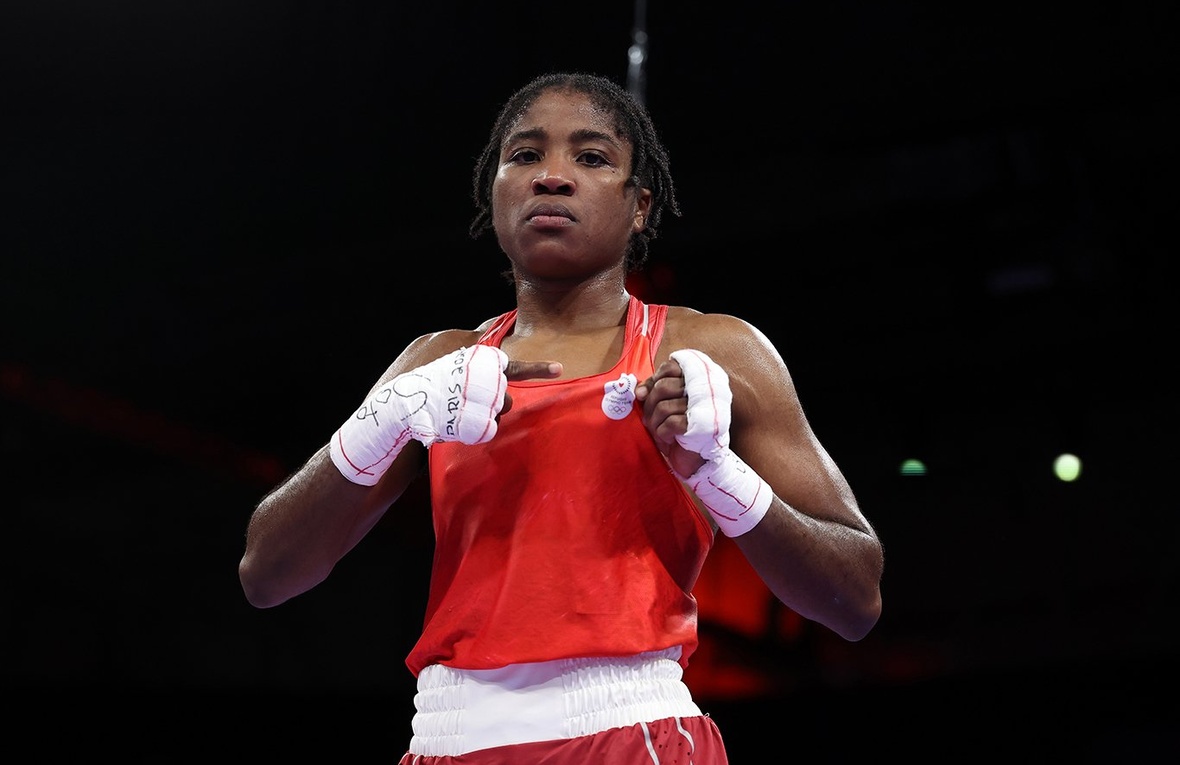Cindy Ngamba poses for a photo in boxing gear, pointing at the Refugee Olympic team logo on her clothes.