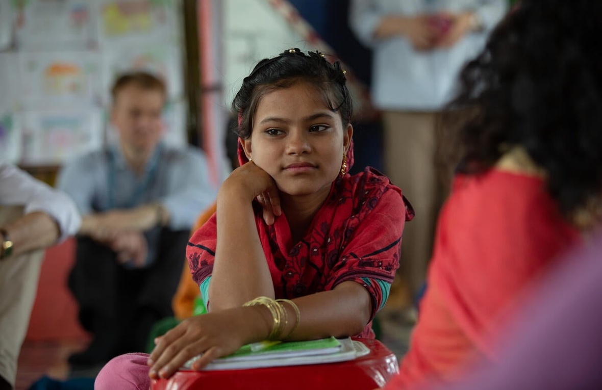 A girl dressed in red looks away from the camera while leaning on a small pile of books