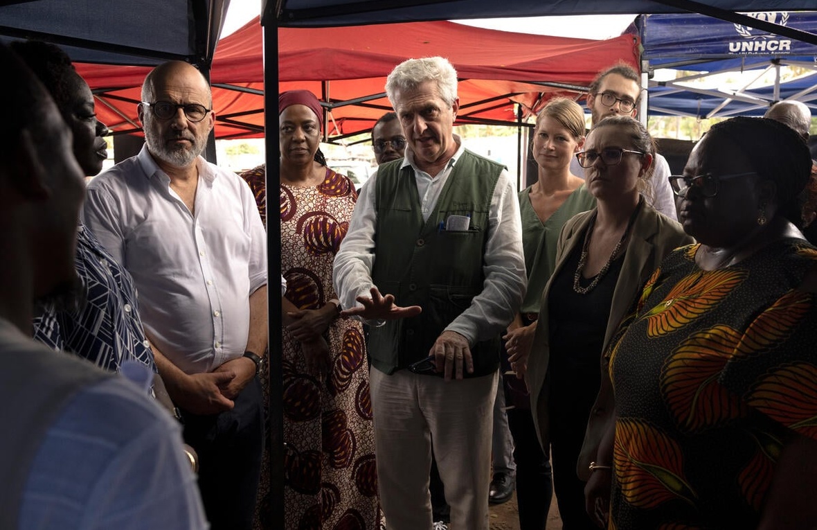 A group of people meet outside under some colored shade cloth