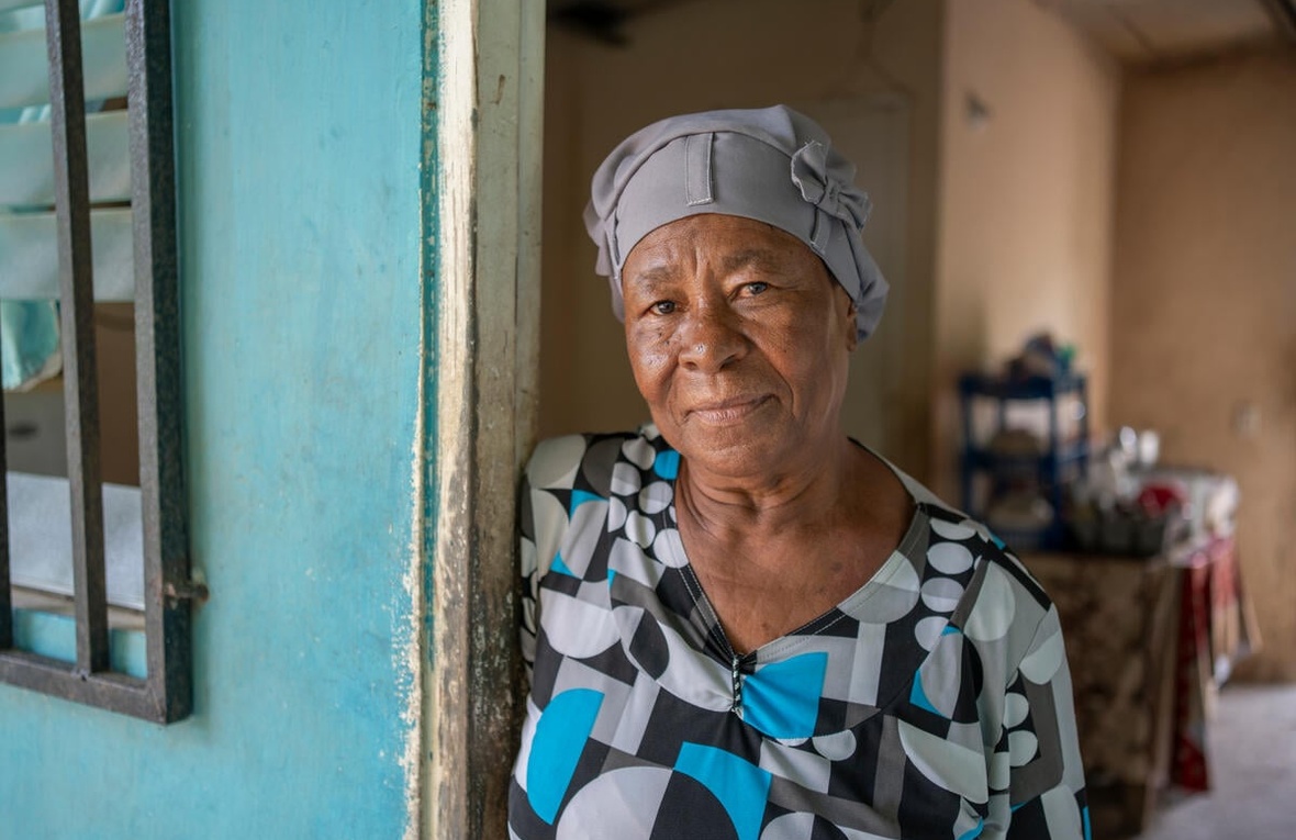An older woman stands in the doorway of a house.