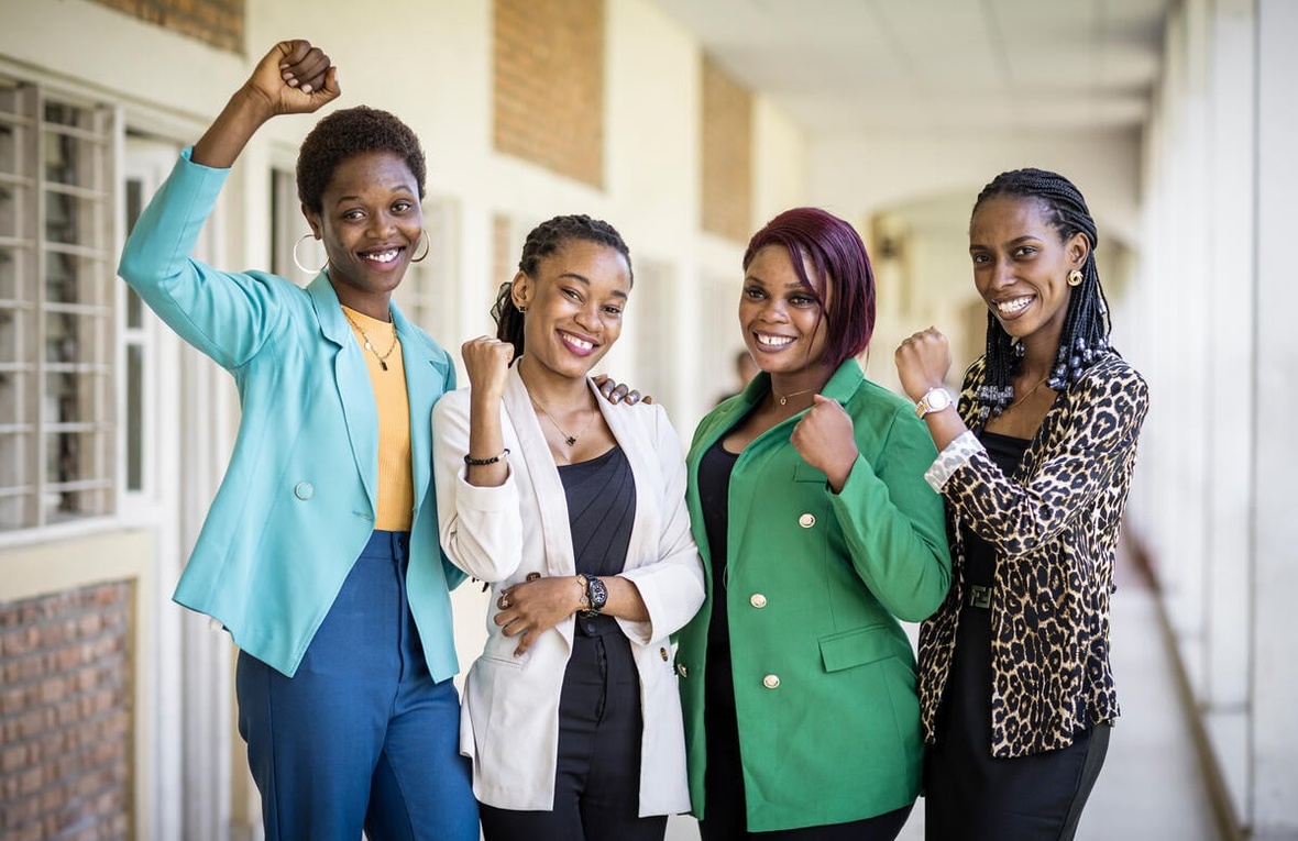 Four women pose with their fists in the air, smiling.