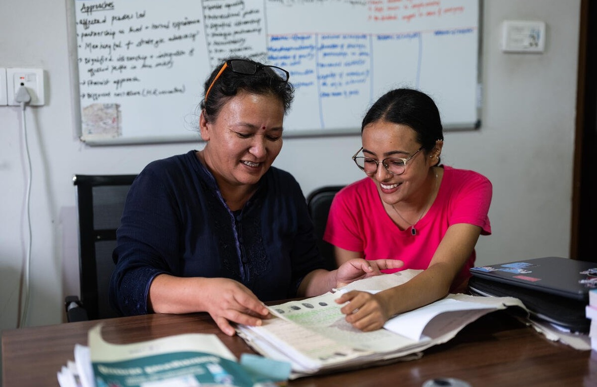 Two women smile as they page through some papers in a file.