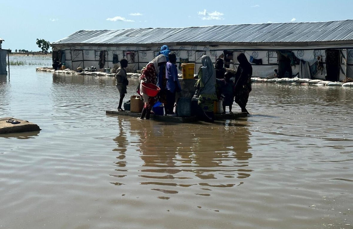 Women and children gather around a water point surrounded by floodwaters.